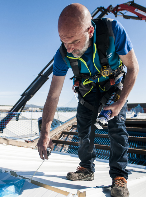 Trabajador en un tejado poniendo pegamento con un spray para que la cubierta del techo se aguante