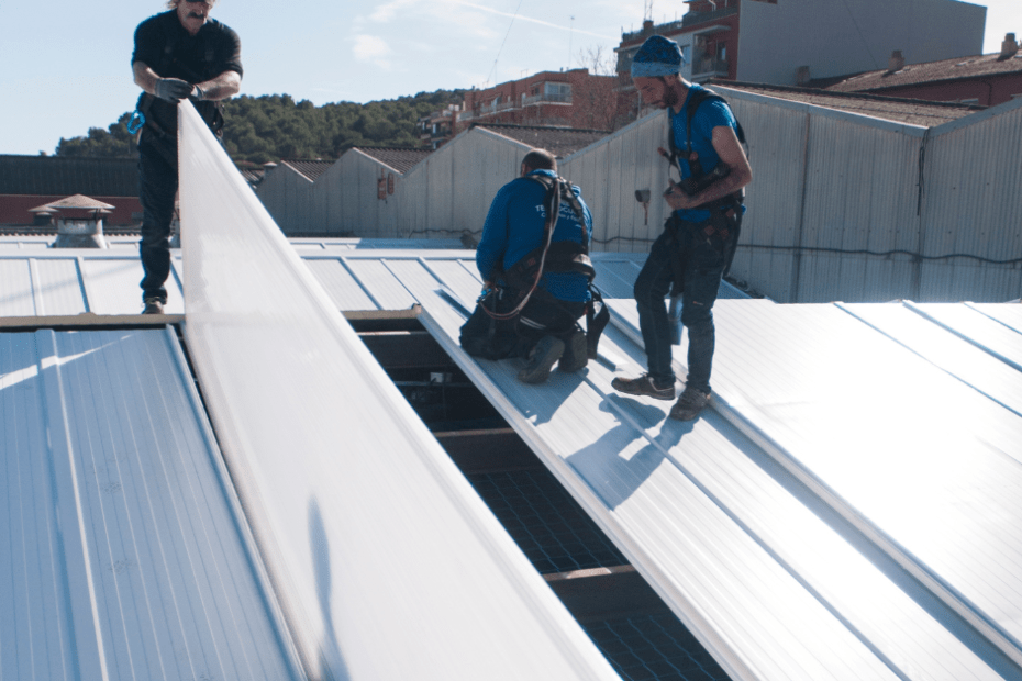Trabajadores subidos al tejado de un edificio con un taladro instalando cubiertas metálicas